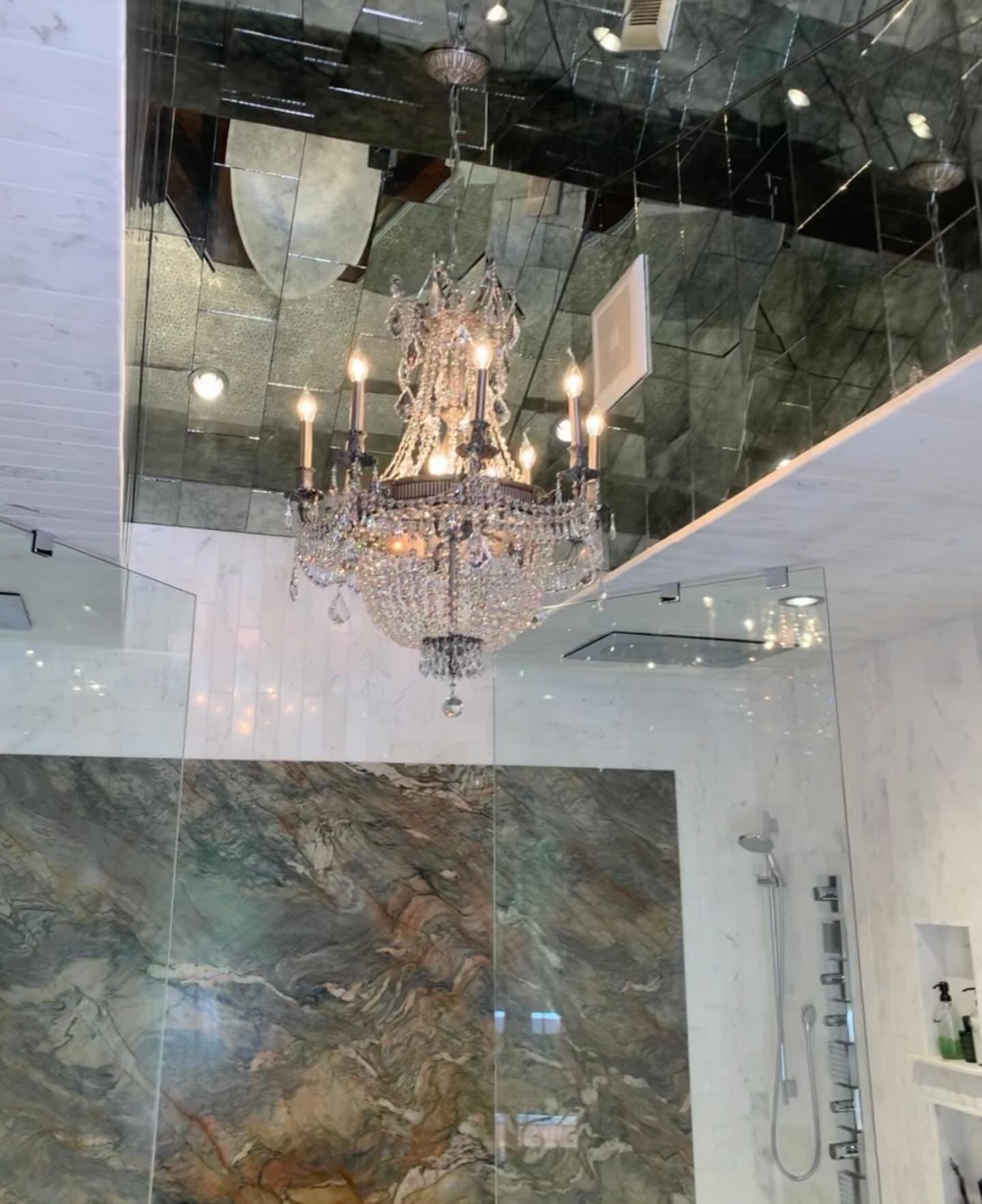 A crystal chandelier hanging in a bathroom with a mirrored ceiling and marble walls