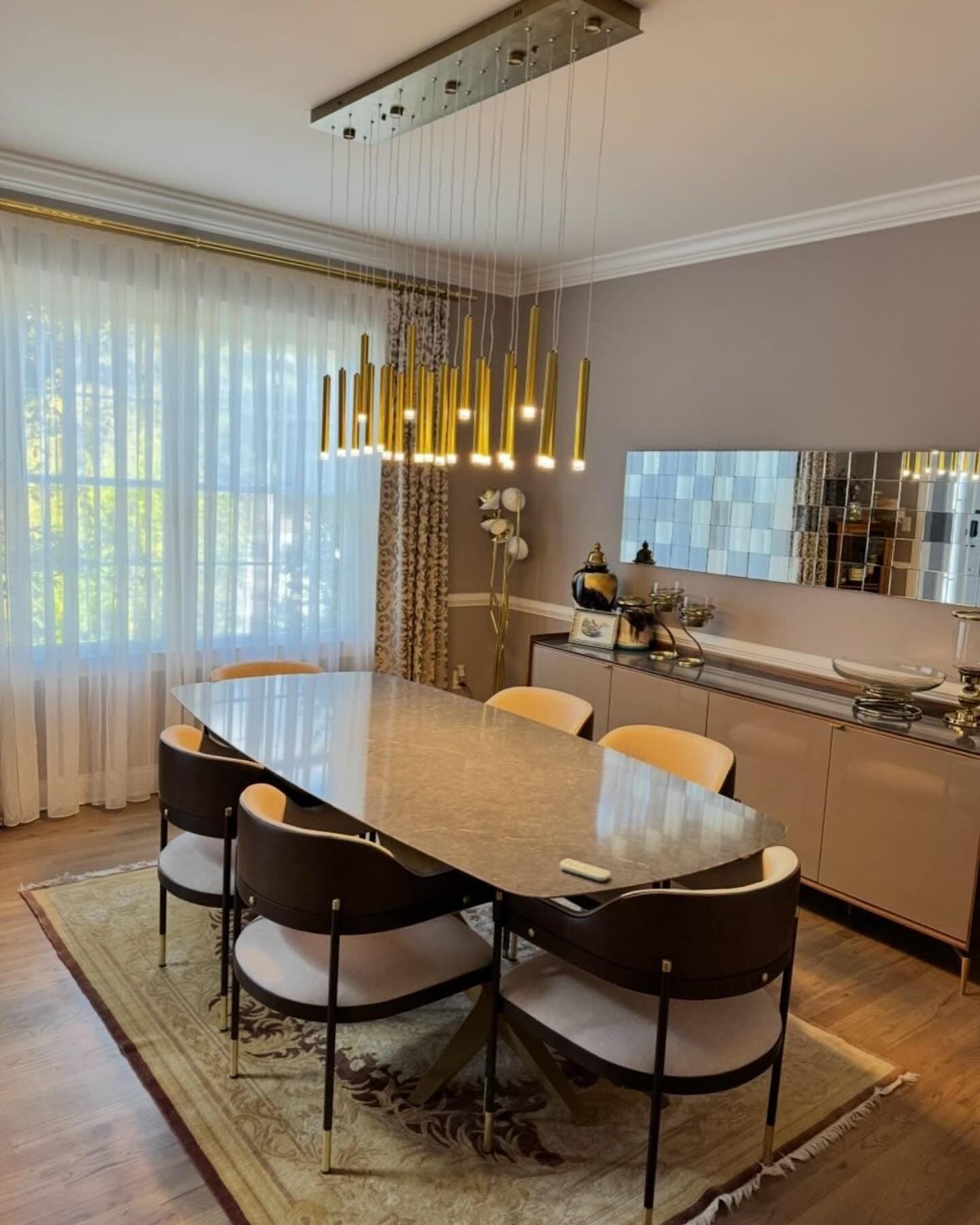 A dining room with a long linear chandelier of gold rods hanging over an oval table