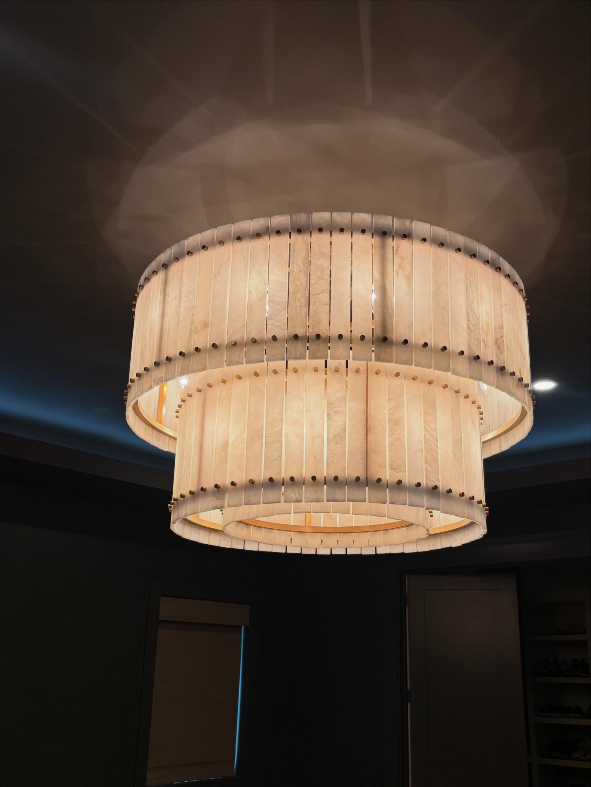 A two-tier drum chandelier lit up under a dark tray ceiling with a glowing cove light