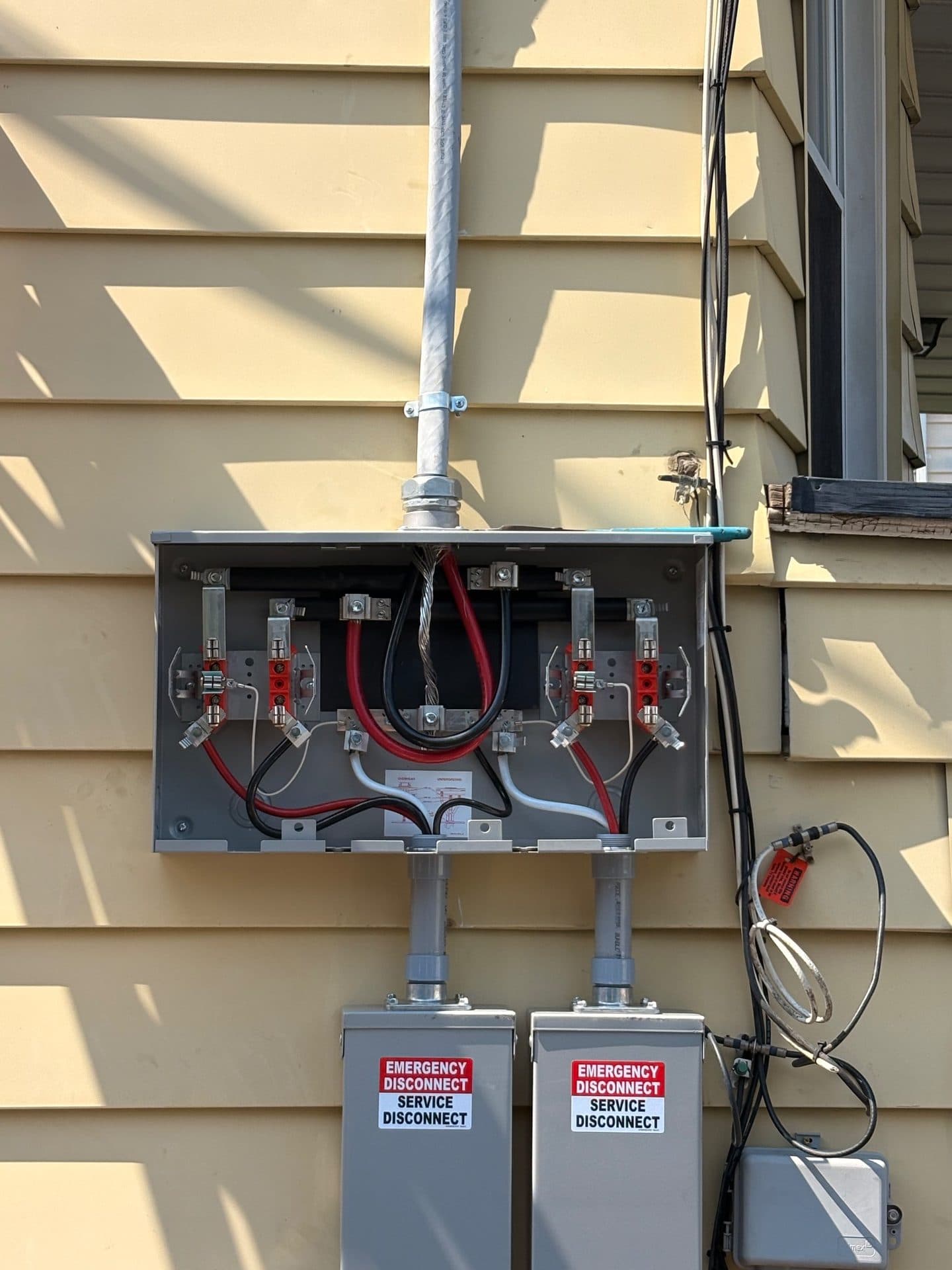 An open two-position meter socket on a house wall with the service wiring visible and two service disconnects mounted below it